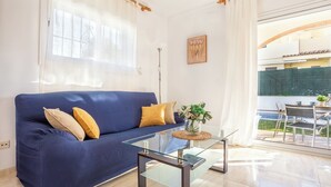 A living room with a blue sofa, a glass coffee table, and a view of an outdoor patio. - Casa Sunset (L'Escala)