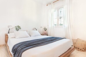 A neatly made bed with a blue blanket, a bedside table with a lamp, and a window with curtains.