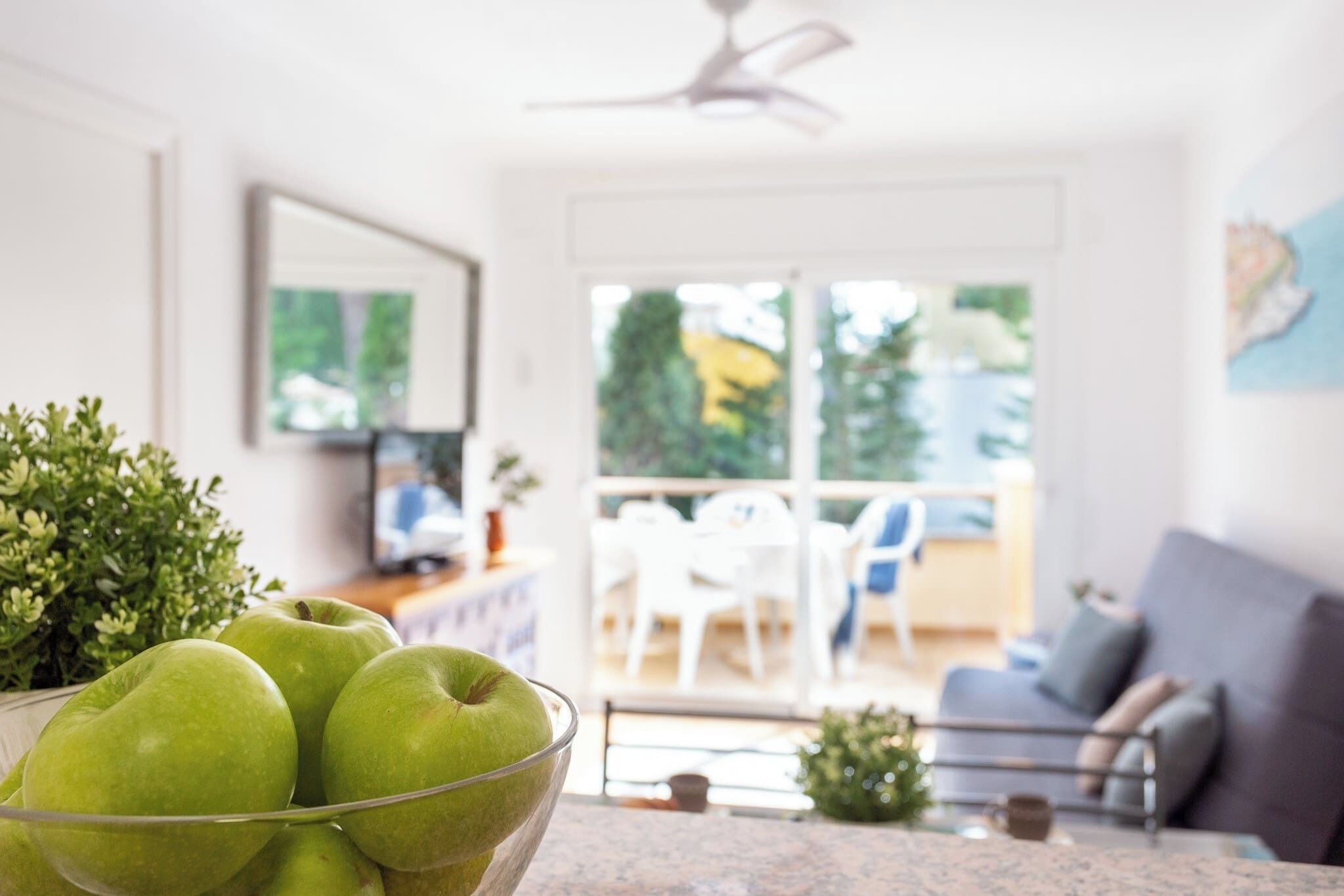 Una cucina moderna con una ciotola di mele verdi sul bancone, una ventola a soffitto e vista sul patio esterno.