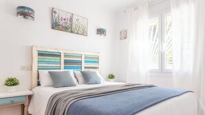 Quarto com cama, mesa de cabeceira, luminária na parede e janela com cortinas.
