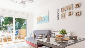 Uma sala de estar moderna com uma mesa de jantar de vidro, sofá cinzento e uma varanda com cadeiras brancas.