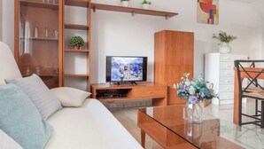 A living room with a sofa, TV, wooden cabinet, and a glass coffee table. - Casa Amapola (L'Escala)