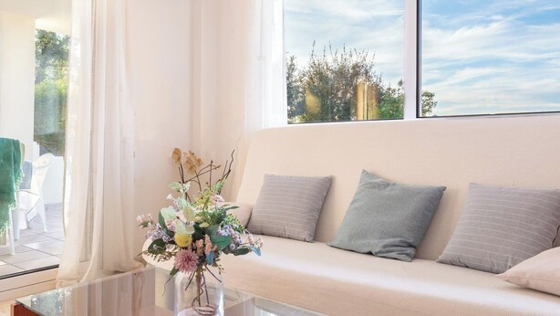 A room with a sofa, a glass table, and a vase with flowers. - Casa Amapola (L'Escala)