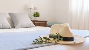 A bed with a hat and green leaves on it, a lamp, and a small plant on a nightstand. - Casa Amapola (L'Escala)