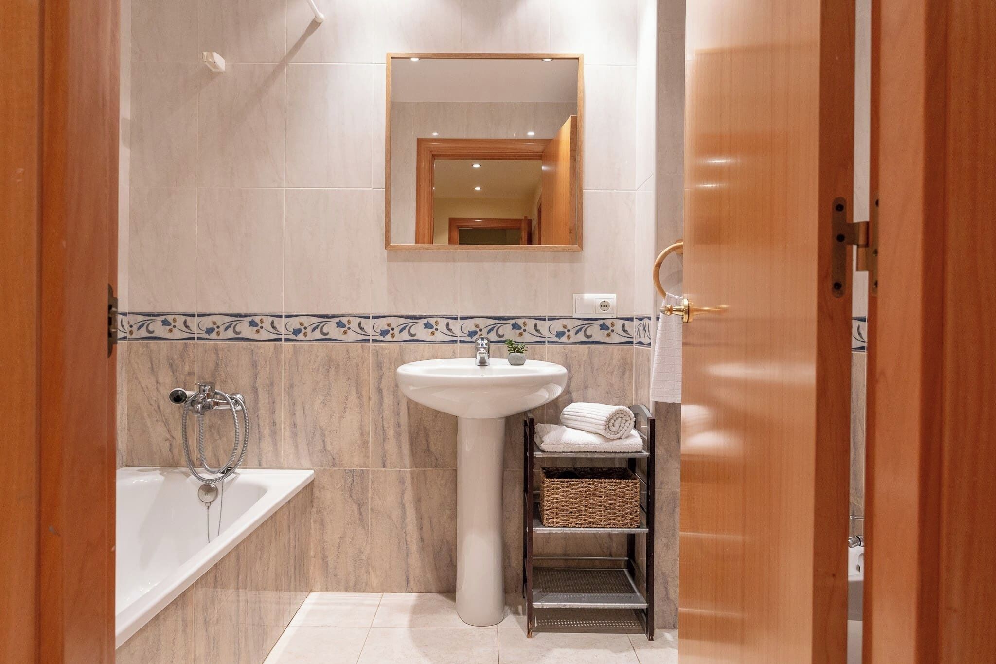 A bathroom with a bathtub, a pedestal sink, a mirror, and a shelf with towels.