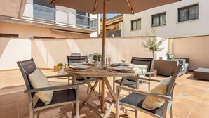 Terrassa exterior amb una taula rodona, cadires i una ombrel·lera.