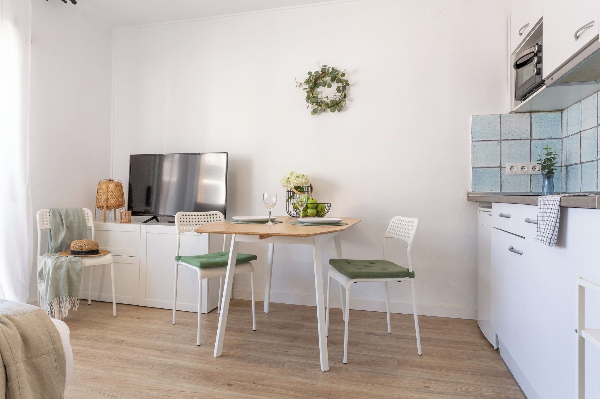 Een moderne keuken met witte kastjes, een houten eettafel en een televisie.