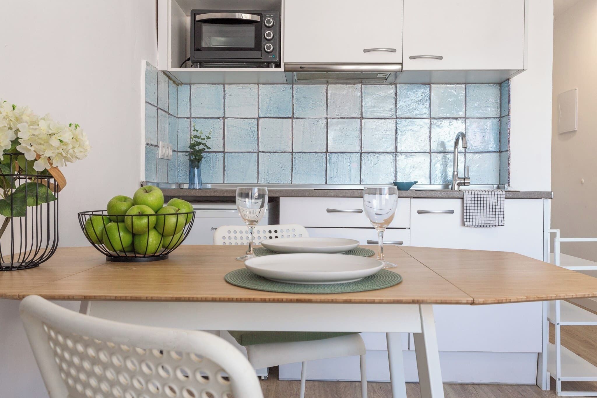 A modern kitchen with a microwave, white cabinets, a tiled backsplash, and a dining table set with plates and glasses.