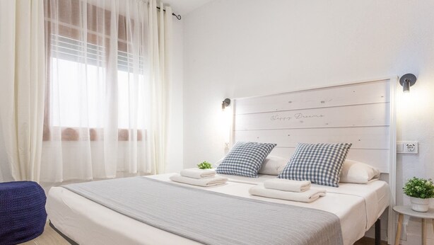 Une chambre à coucher avec un grand lit, une table de chevet avec une lampe et une fenêtre ornée de rideaux légers.