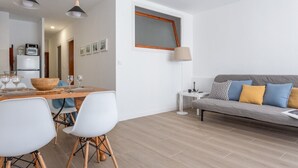 Un salon moderne avec un canapé gris, des chaises blanches, une table à manger en bois dressée pour quatre personnes et des luminaires suspendus.