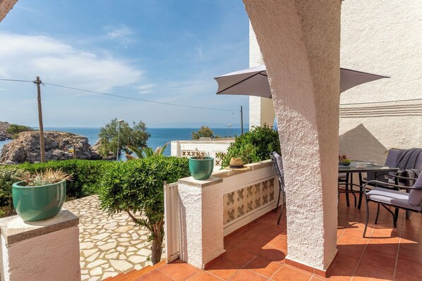 A patio with a view of the sea, a table with chairs, and potted plants.
