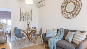 A modern living room with a grey sofa, blue and striped pillows, a round mirror, and a dining area with a wooden table and chairs. - Bohemia Apartment with Terrace (L'Escala)