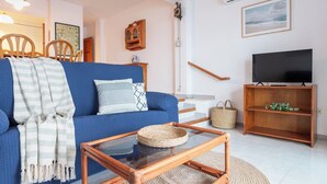 Un salon avec un canapé bleu, une table basse en verre, un meuble TV en bois et un escalier.