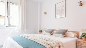 Une chambre à coucher bien rangée, avec un lit, des tables de chevet et une fenêtre avec des rideaux.