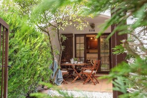 A cozy outdoor seating area with a table and chairs, surrounded by lush greenery and a white pebble path. - Apt. Clover (L'Escala)