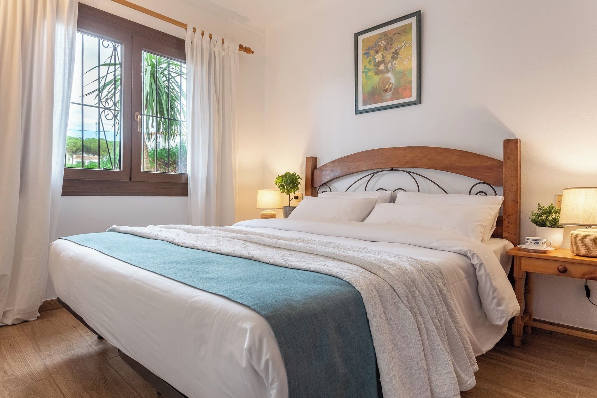 A neatly made bed with a wooden headboard, a bedside table with a lamp, and a window with curtains.