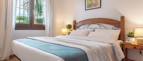 A neatly made bed with a wooden headboard, a bedside table with a lamp, and a window with curtains.