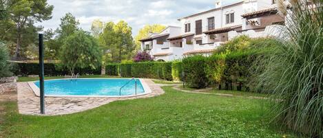 Une piscine entourée d’une pelouse bien entretenue et de haies, avec une grande maison en arrière-plan.