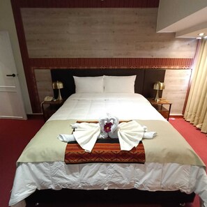 A hotel room with a large bed, two bedside tables with lamps, a wooden headboard, and a red carpet.