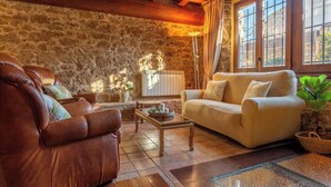 A cozy living room with stone walls, a wooden ceiling, a beige sofa, a brown leather armchair, and a small table with decorative items. - Rural House Salvador XVIII (La Tallada d'Empordà)