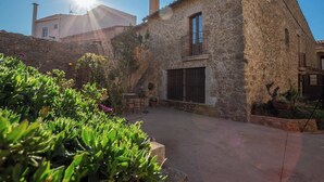 A stone building with a large window and a balcony, surrounded by greenery and a paved area. - Rural House Salvador XVIII (La Tallada d'Empordà)
