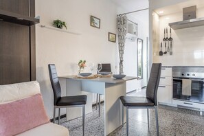 A modern kitchen with a central island, two bar stools, a dining table, and a sofa with cushions.