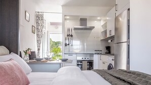 Ein modernes Schlafzimmer mit einem großen Bett, einem kleinen Schreibtisch mit Stuhl und Blick auf eine Küchenzeile.