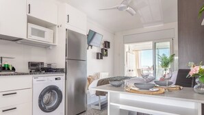 Eine moderne Küche mit eingebautem Waschmaschinen, einer Mikrowelle und einem Kühlschrank. Es gibt einen Essbereich mit einem Tisch für zwei Personen, und ein an der Wand montierter Fernseher.