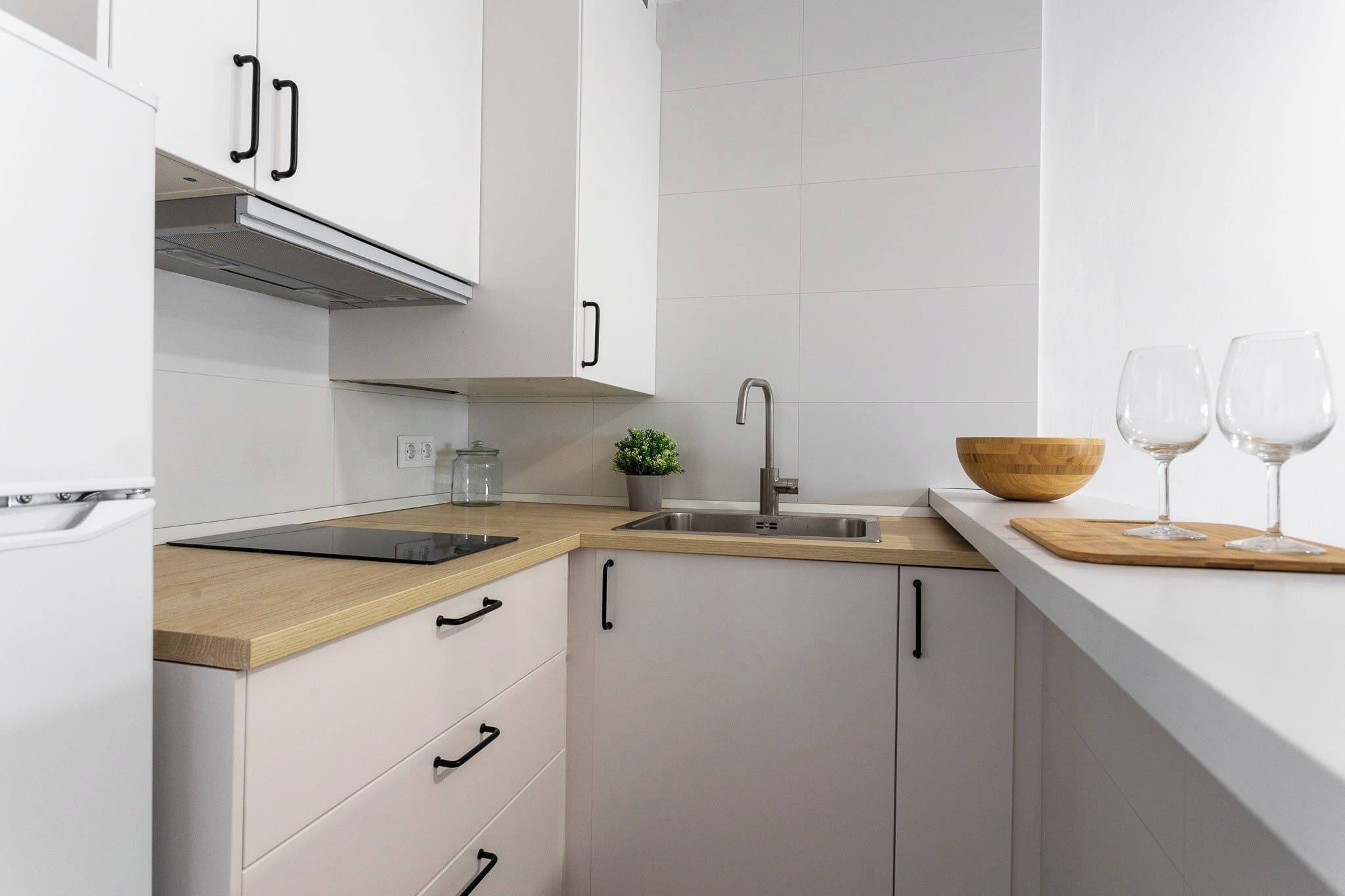 Une cuisine moderne avec des meubles blancs, un plan de travail en bois, un évier en acier inoxydable et une petite plante en pot.