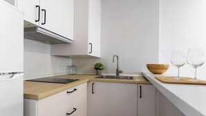 Une cuisine moderne avec des meubles blancs, un plan de travail en bois, un évier en acier inoxydable et une petite plante en pot.