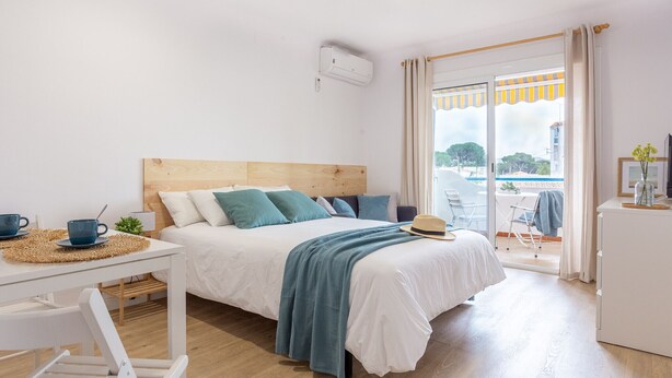Une chambre d’hôtel moderne avec un lit doté d’une tête de lit en bois, une literie blanche et une vue à travers la porte vitrée.
