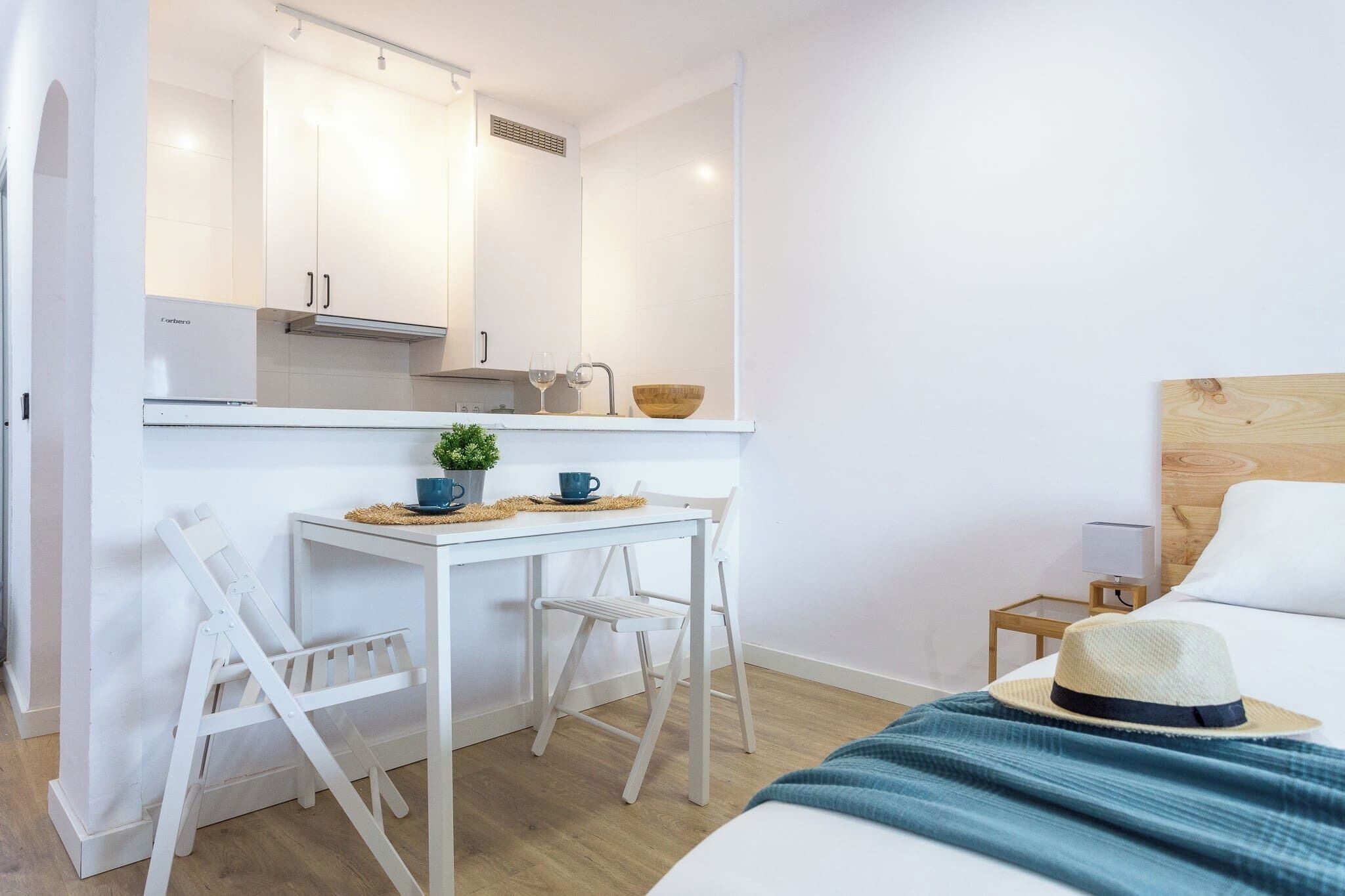 Une chambre d’hôtel compacte comprenant un coin cuisine, un lit, une petite table de chevet et une chaise.