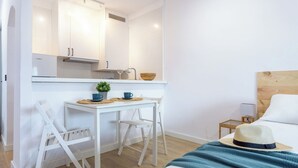 Une chambre d’hôtel compacte comprenant un coin cuisine, un lit, une petite table de chevet et une chaise.