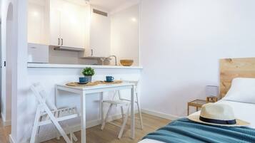 Une chambre d’hôtel compacte comprenant un coin cuisine, un lit, une petite table de chevet et une chaise.