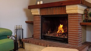 A fireplace with a brick surround and a mantel, a green armchair, and a candle holder. - Casa Quimeta (L'Escala)
