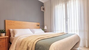 A neatly made bed with a wooden headboard, a bedside table with a lamp, and a window with sheer curtains. - Casa Quimeta (L'Escala)