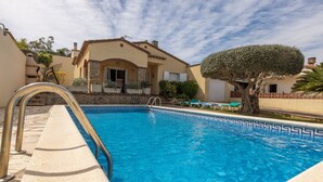 A swimming pool with a stone deck, a tree, and a building with a tiled roof. - Casa Quimeta (L'Escala)