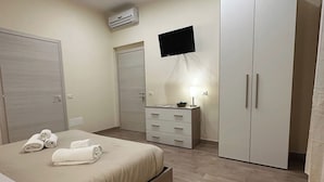 A modern bedroom with a bed, a TV mounted on the wall, a wardrobe, and a bedside table with a lamp. - Double Room with private bathroom for the disabled in Terralba (Oristano) – Olivo (Terralba)