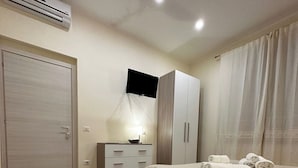 A bedroom with a bed, a TV mounted on the wall, a wardrobe, and an air conditioning unit. - Double Room with private bathroom for the disabled in Terralba (Oristano) – Olivo (Terralba)