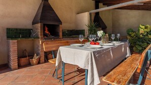 An outdoor dining area with a brick oven, wooden benches, and a table set for a meal.