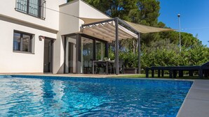 Une piscine avec un patio couvert, une table à manger et des sièges d’extérieur.