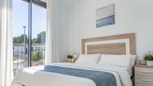 Une chambre avec un grand lit, une tête de lit en bois, une table de chevet avec une lampe et une vue sur l’extérieur.