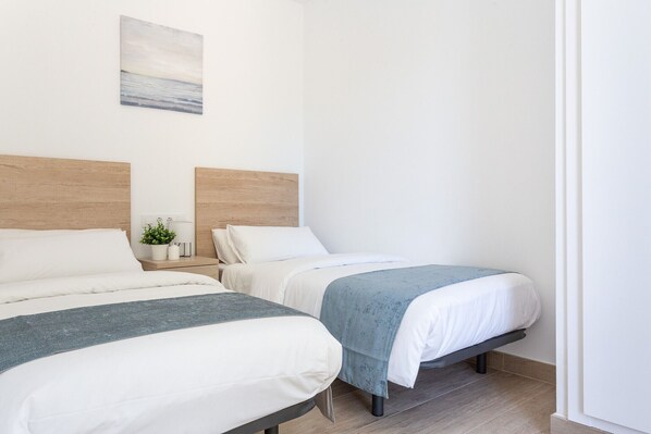 Una habitación de hotel con dos camas, una mesita de noche con una planta y un cuadro en la pared.