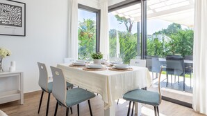 Un coin repas avec une table dressée pour quatre personnes, de grandes fenêtres et une vue sur la verdure environnante.