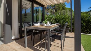 Un espace de restauration en plein air avec une table dressée pour quatre personnes, entourée de chaises en osier, sous une pergola.