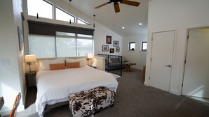A spacious bedroom with a large bed, a ceiling fan, and a view of the outdoors through large windows. - Cozy 1-bedroom cottage with outdoor fire pit (Kyle)