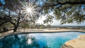 A swimming pool with clear blue water, surrounded by stone tiles and a wooden deck. - Cozy 1-bedroom cottage with outdoor fire pit (Kyle)