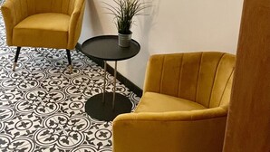 Ett rum med två gula fåtöljer, ett litet runt bord med en växt och en stor, abstrakt målning på väggen.