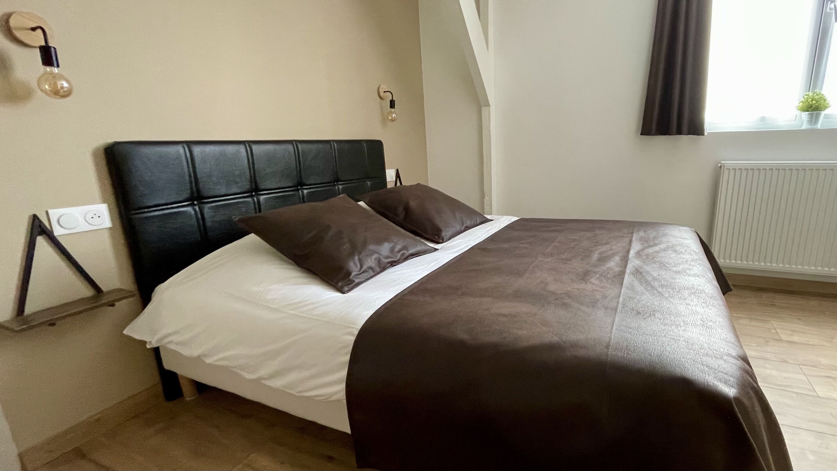 A neatly made bed with a black headboard, white linens, and two brown pillows.