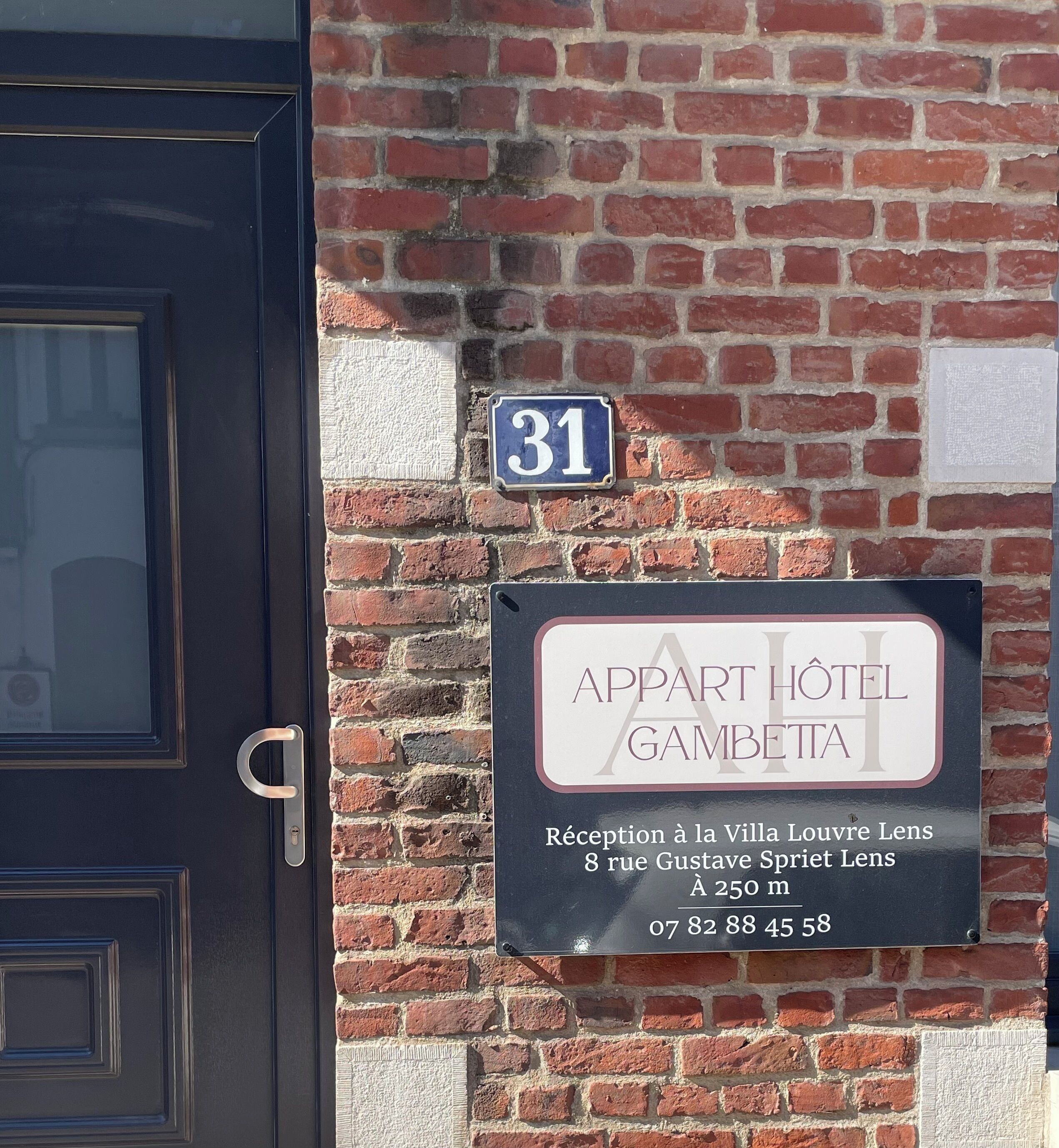 Paret de maó amb una porta i dos senyals: un indica el número 31 i l'altre per 'Appart Hotel Gambetta' amb recepció a Villa Louvre Lens.
